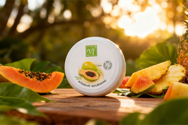 تصویر کرم نوتری تاچ مای در کنار میوه&zwnj;های استوایی و برگ&zwnj;های سبز