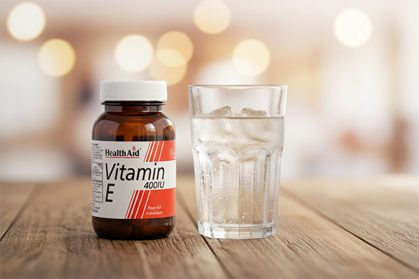 کپسول ویتامین E 400 هلث اید کنار لیوان آب