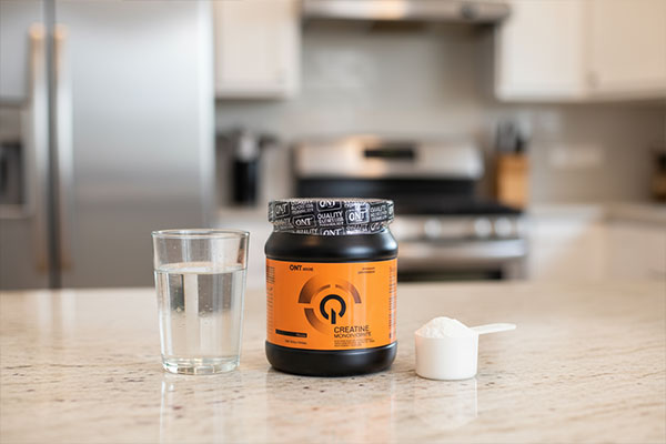 پودر کراتین مونوهیدرات کیو ان تی 300 گرمی در کنار لیوان آب