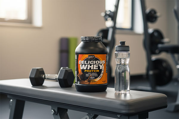 پودر پروتئین دلیشس وی کیو ان تی در کنار تجهیزات ورزشی