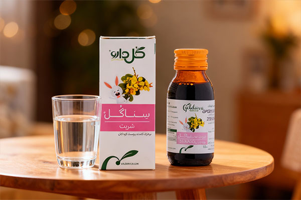 شربت سناگل گل دارو کنار لیوان آب روی میز چوبی