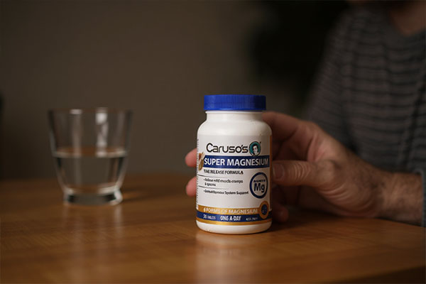 تصویر قرص سوپر منیزیم در دست شخص با لیوان آب در پسزمینه